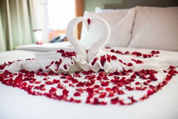 istockphoto-957093966-612×612 two swans made from towels are kissing on honeymoon white bed. creamy pillow and heart form, valentine signature made from red rose flower on bed decoration in bedroom.Valentine background.honey moon